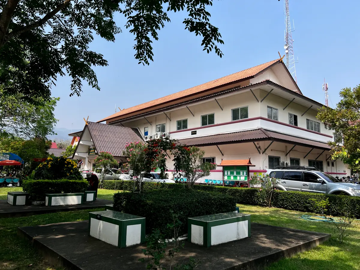 Two-storey office building with a tiled roof among trees, with a parked car.