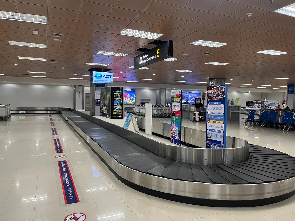 Baggage reclaim hall at Chiang Mai International Airport with a conveyor belt and overhead signs.