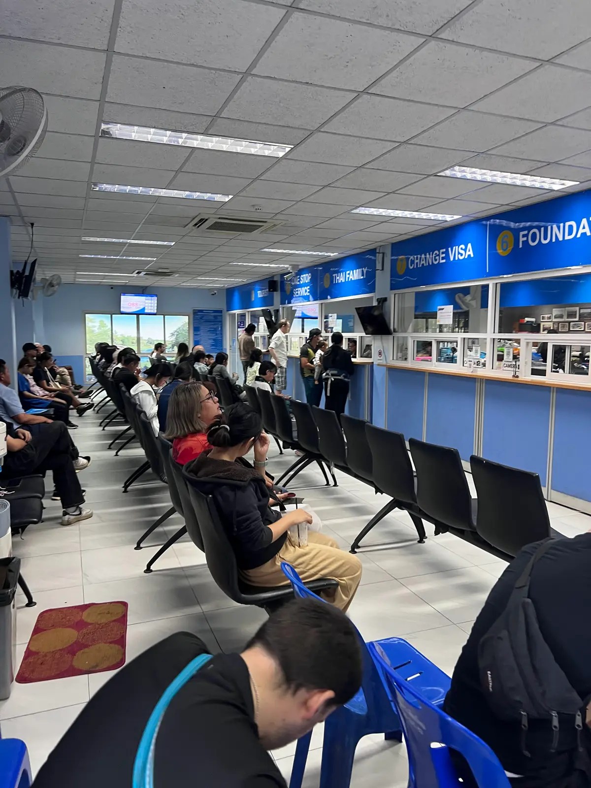 Visitor hall at Chiang Mai Immigration with blue service counters, a Change Visa sign and people waiting in the seating area.