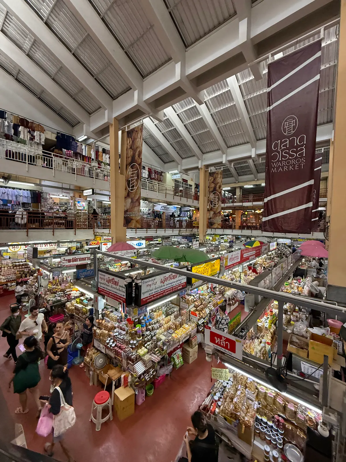 Open-sided market hall with balconies on several levels, hanging banners and crowded stalls on the ground floor.
