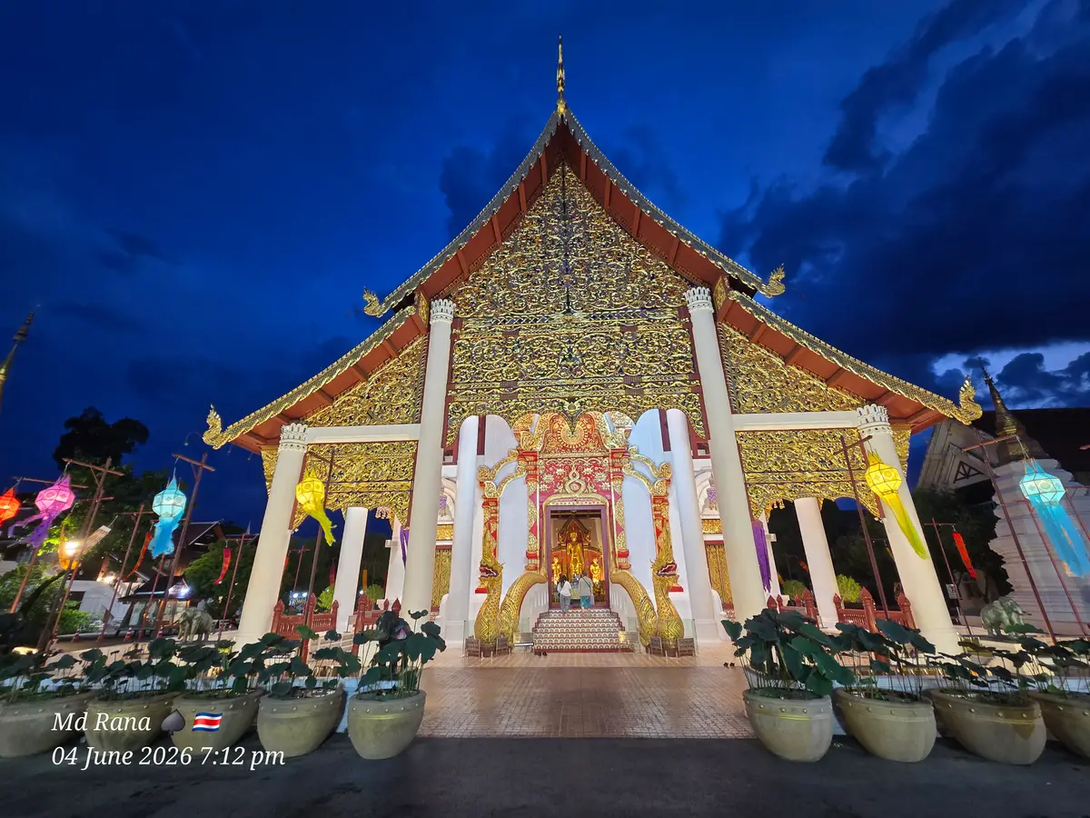 Hall with a golden gable lit up at night, white columns and hanging lanterns