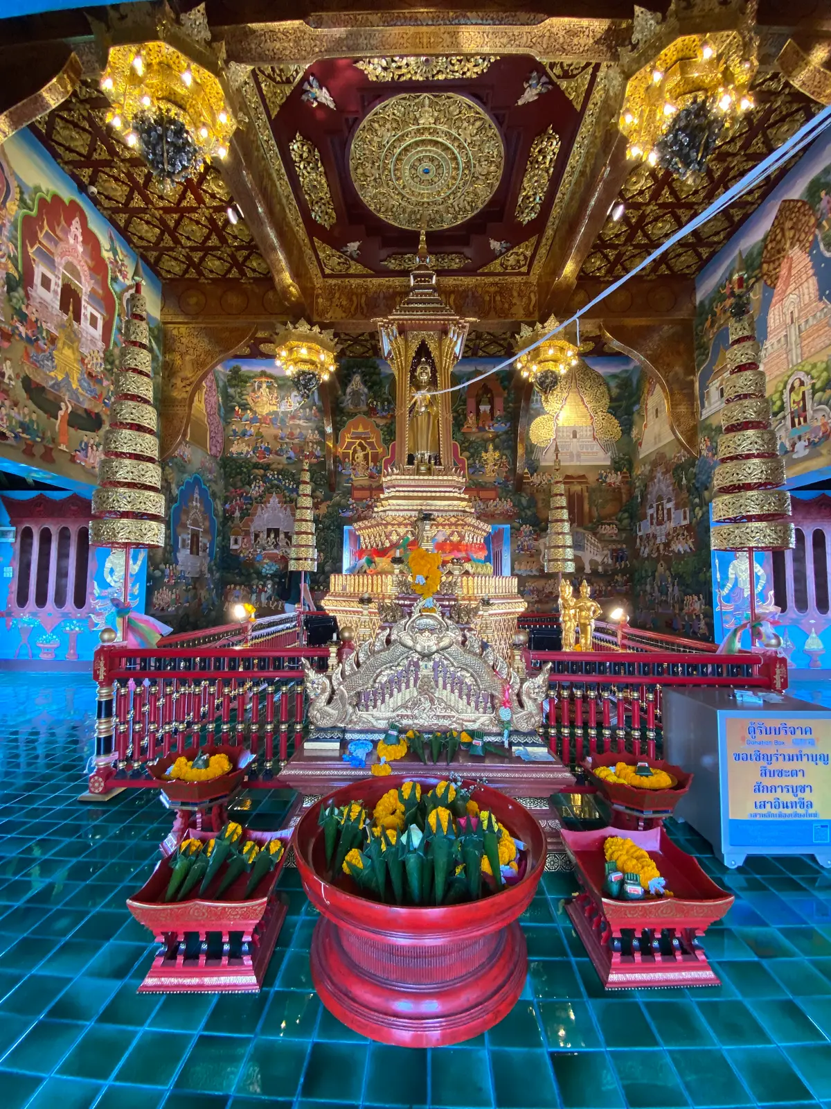 Small silver-and-white spired shrine inside a room with painted walls and flower offerings