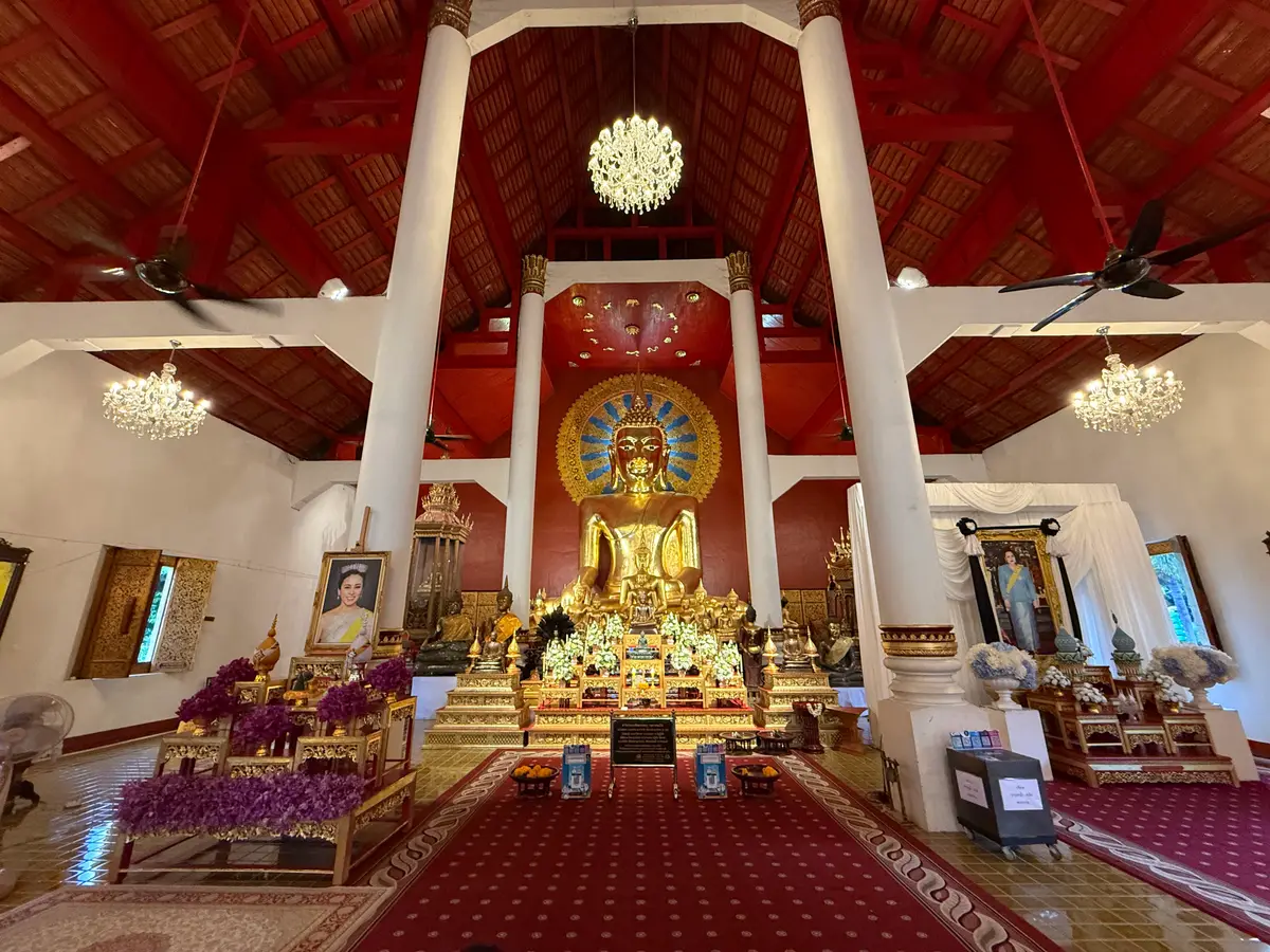 Hall with white columns, a red ceiling and a golden Buddha at the far end behind purple flowers