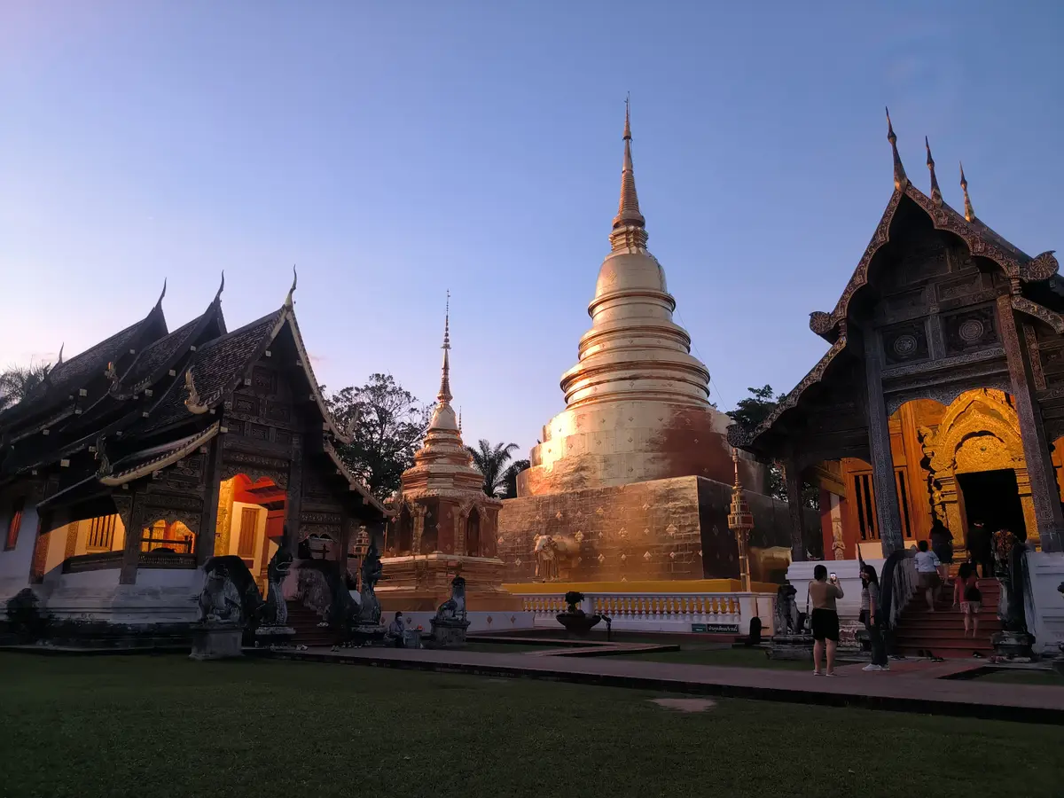 Gold chedi at dusk between two dark wooden temple roofs