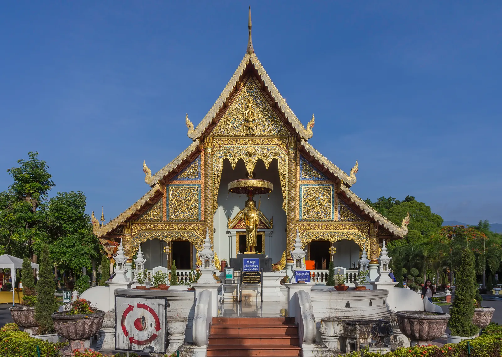 Gilded temple front with a tiered roof and a golden standing figure under a blue sky
