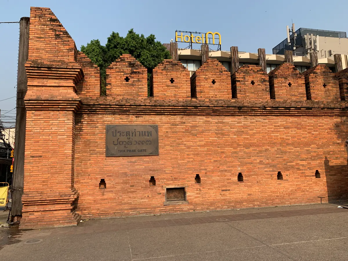 Red brick city gate and wall with a name plaque, seen from the street
