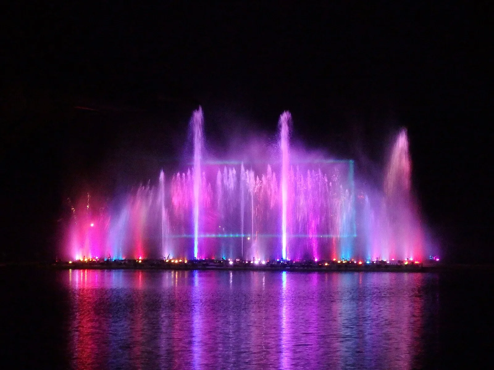 Pink and purple water jets lit up at night over a lake